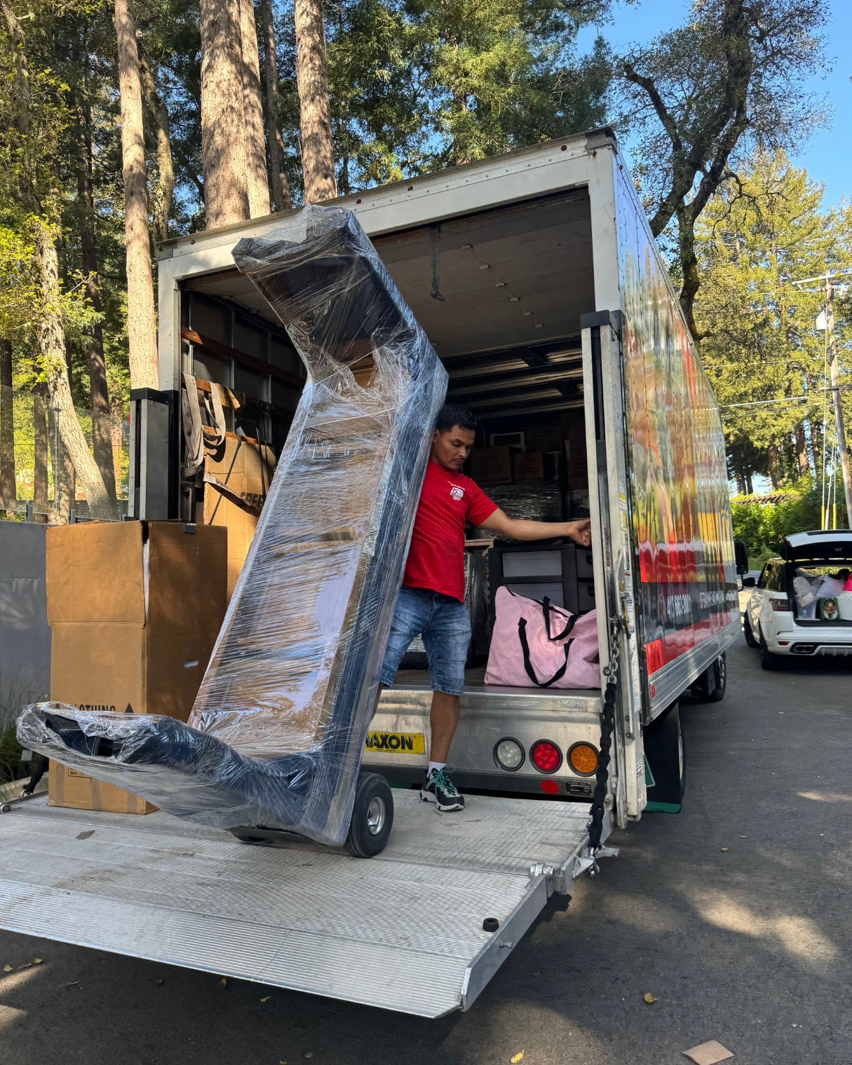 Mover unloading a large fully wrapped furniture item from a residential moving truck