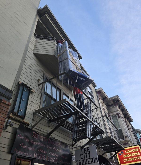 Moving crew carrying a wrapped large furniture item down an exterior apartment staircase