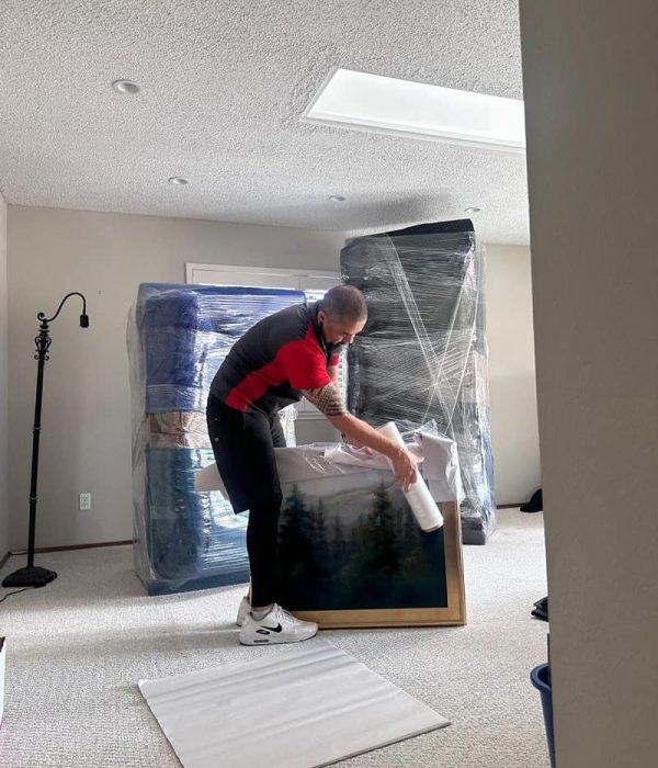 Professional mover carefully wrapping framed artwork for residential transport