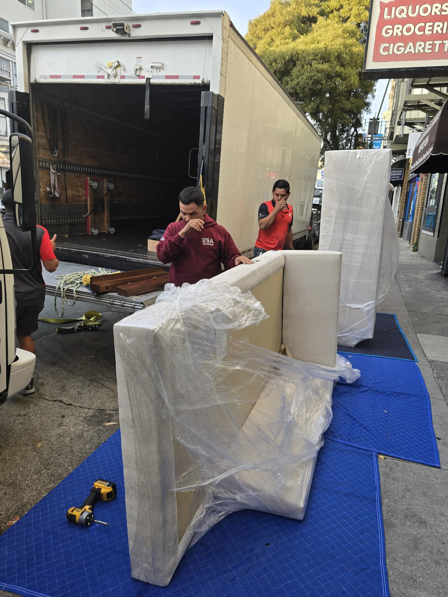 Two SF Bay Area Moving crew members preparing wrapped furniture beside the truck.