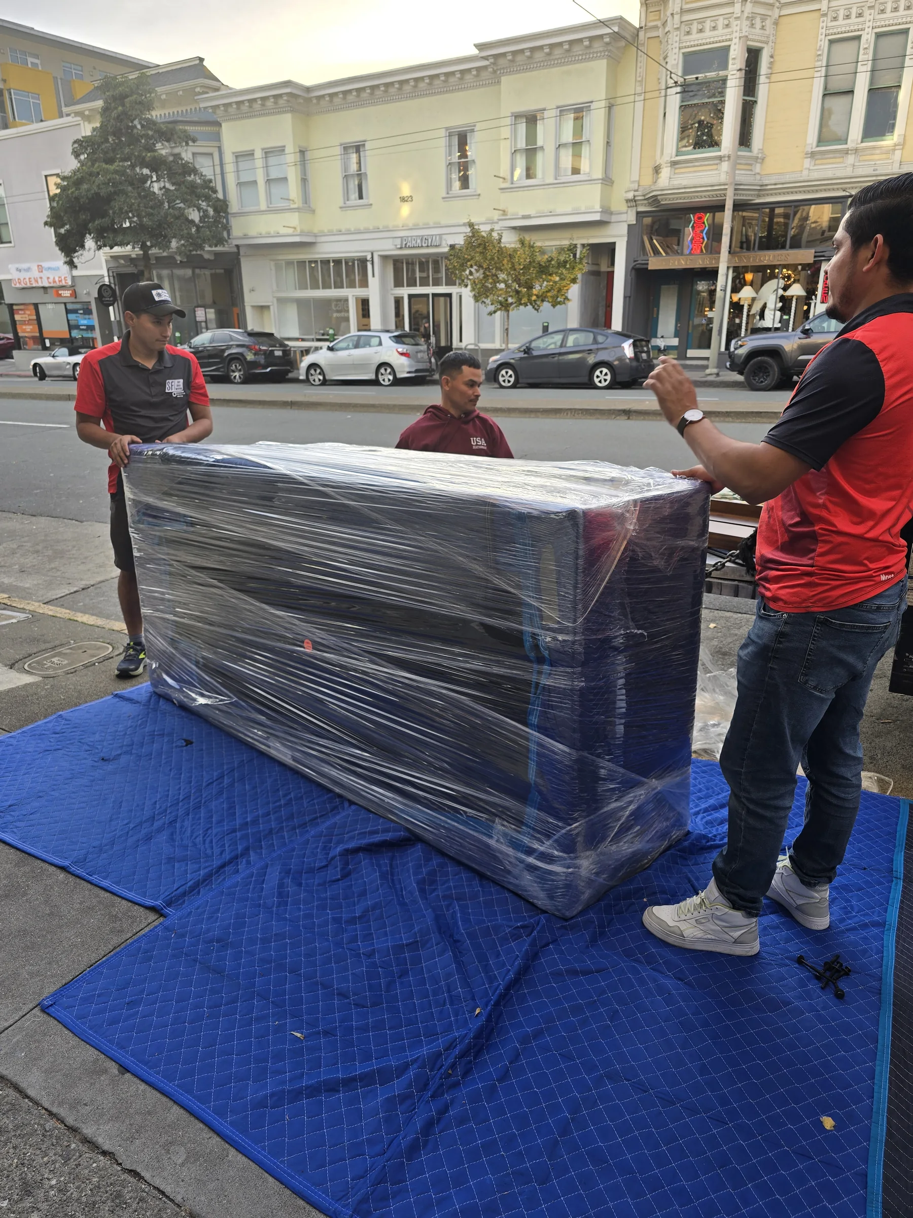 SF Bay Area Moving crew carrying a large wrapped cabinet on a city sidewalk.