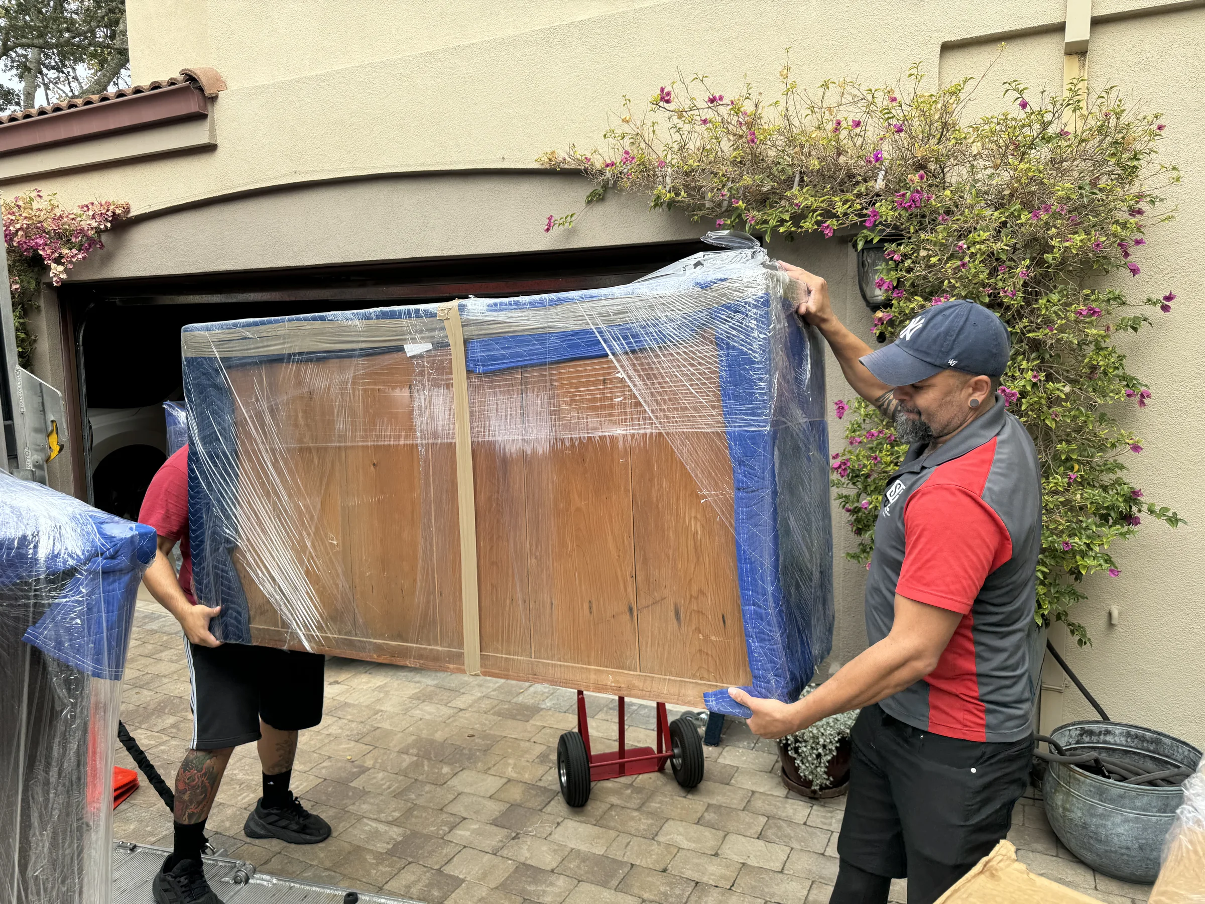 SF Bay Area Moving crew carrying a wrapped wooden cabinet in a residential driveway.