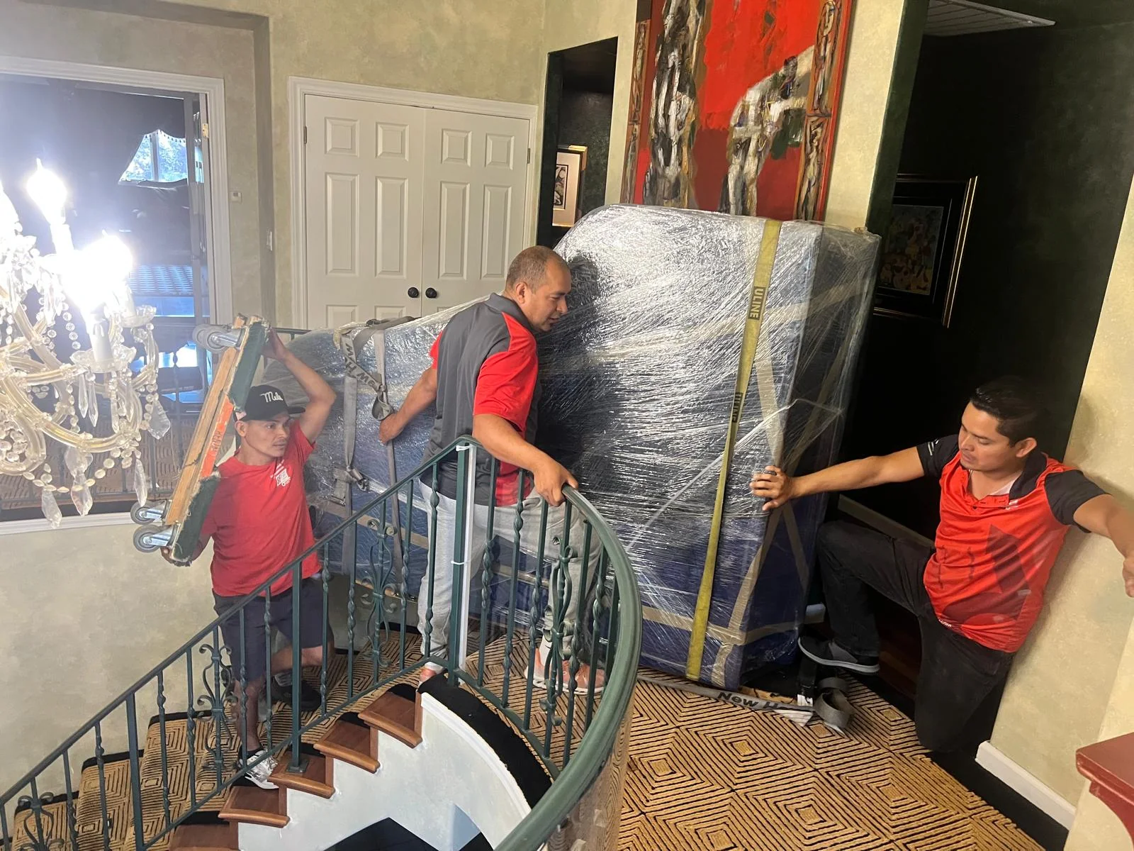 SF Bay Area Moving crew carrying a wrapped cabinet down an interior staircase.